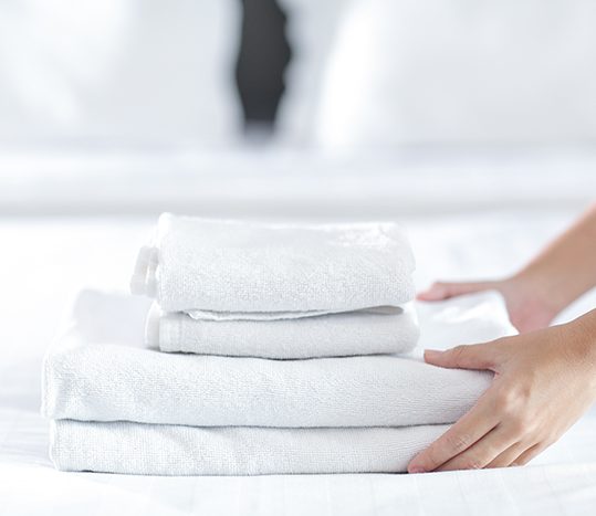Close-up of hands putting stack of fresh white bath towels on th