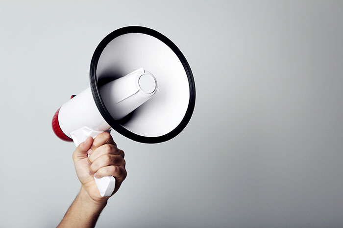 Female hand holding megaphone on grey background